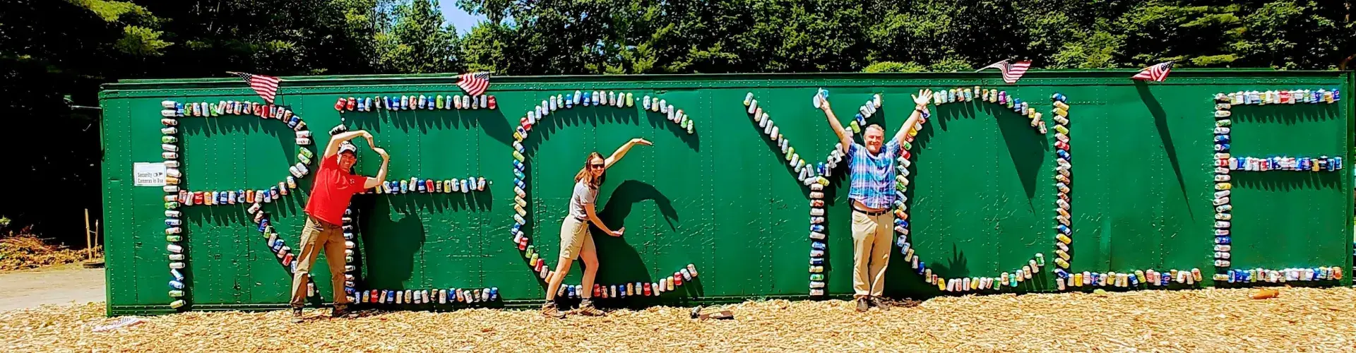 Word "Recycle" written on a wall with three people posing in front of it