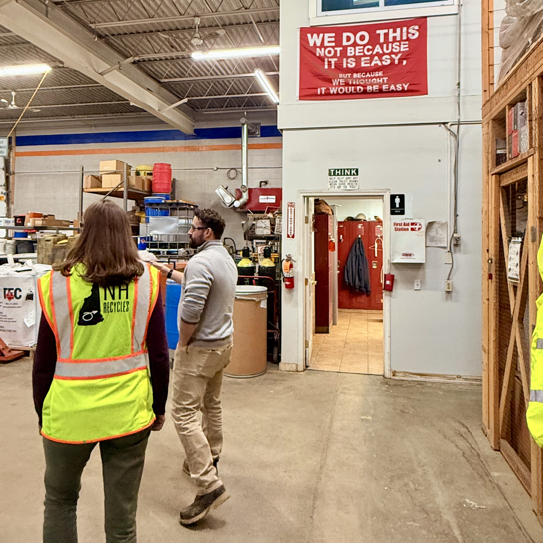 Man and woman walking in an HHW warehouse with funny flag reading "we do this not because it is easy, but because we thought it would be easy."