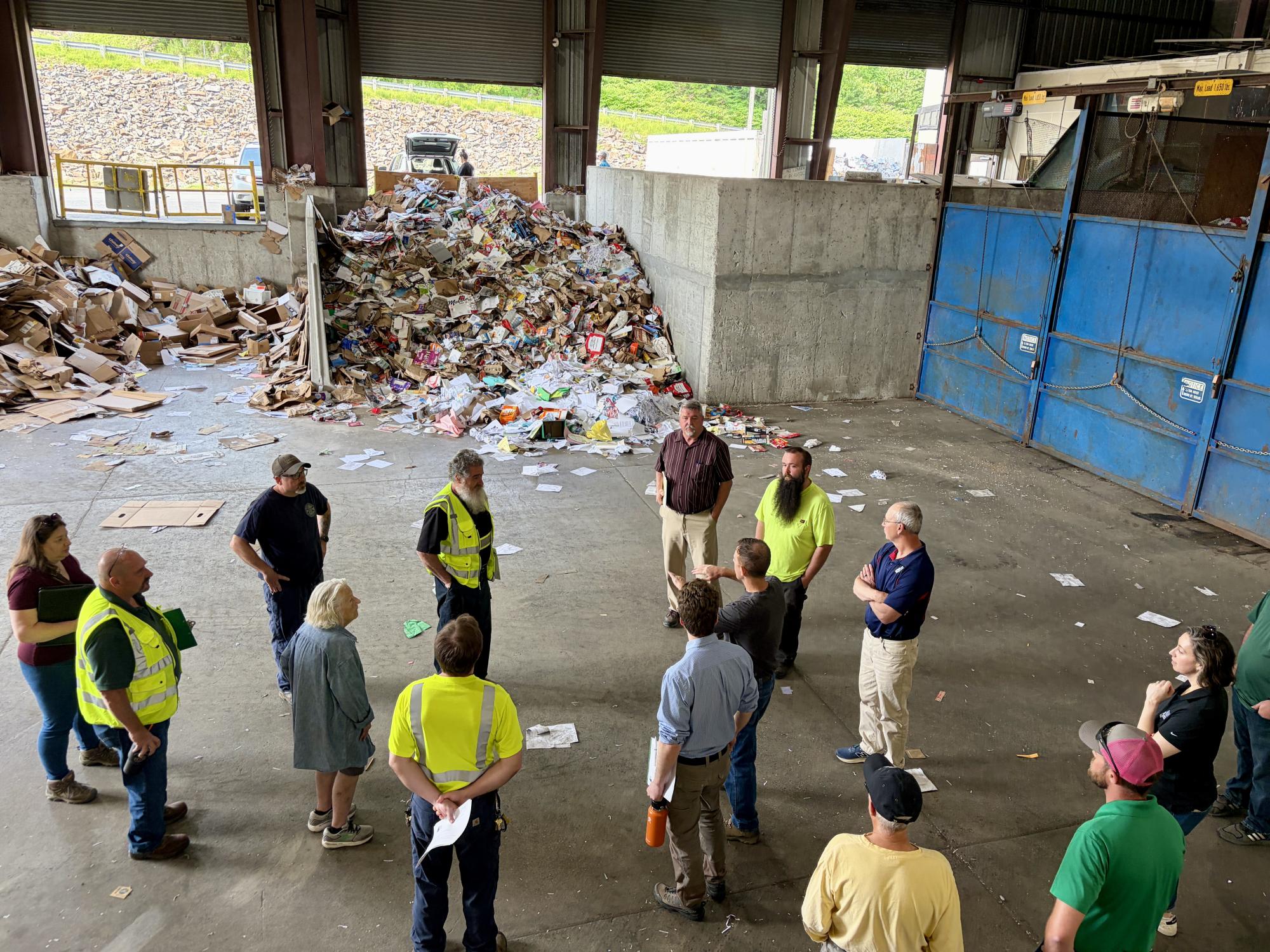 group of people listening to a tour in a recycling facility with paper recycling in the background