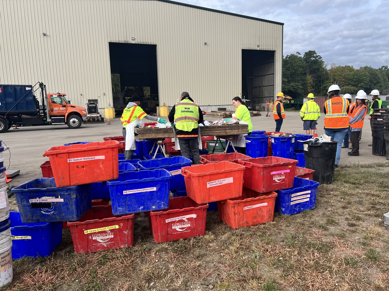 Several red and blue bins with people sorting trash in the background