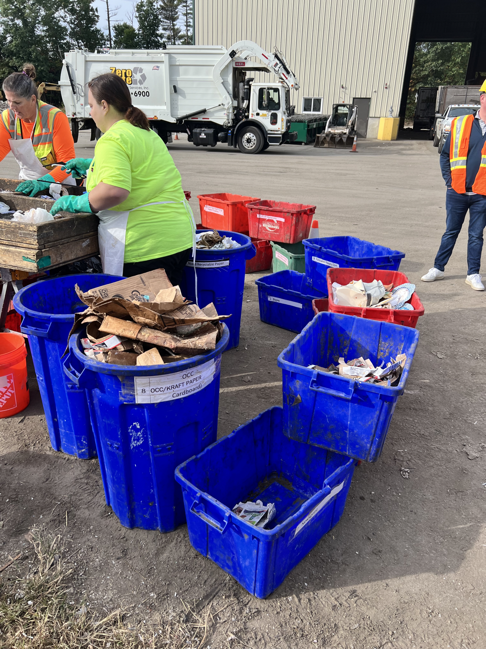 people sorting trash into several blue bins